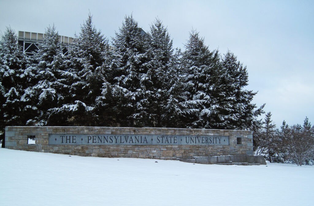 The Pennsylvania State University landmark sign infront of Beaver Stadium on a snowy winter day.